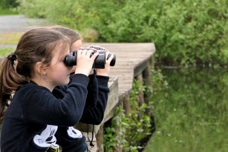 Kinderen met verrekijker op vlonder aan water