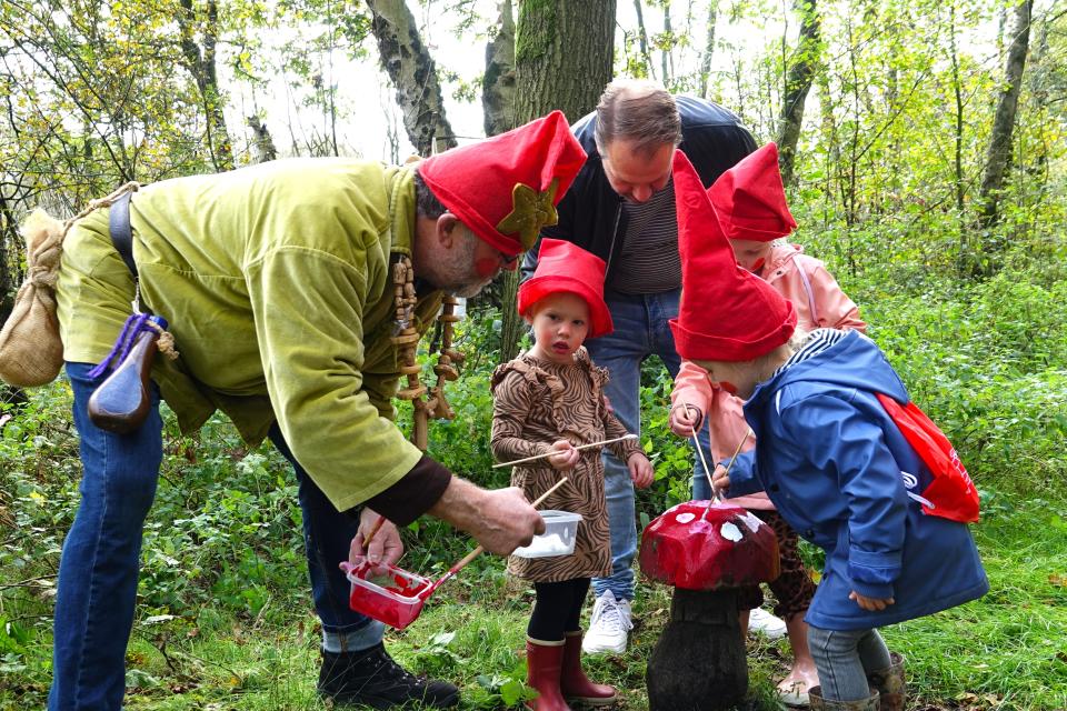 Kinderen en man met kaboutermutsen schilderen paddenstoel in bos