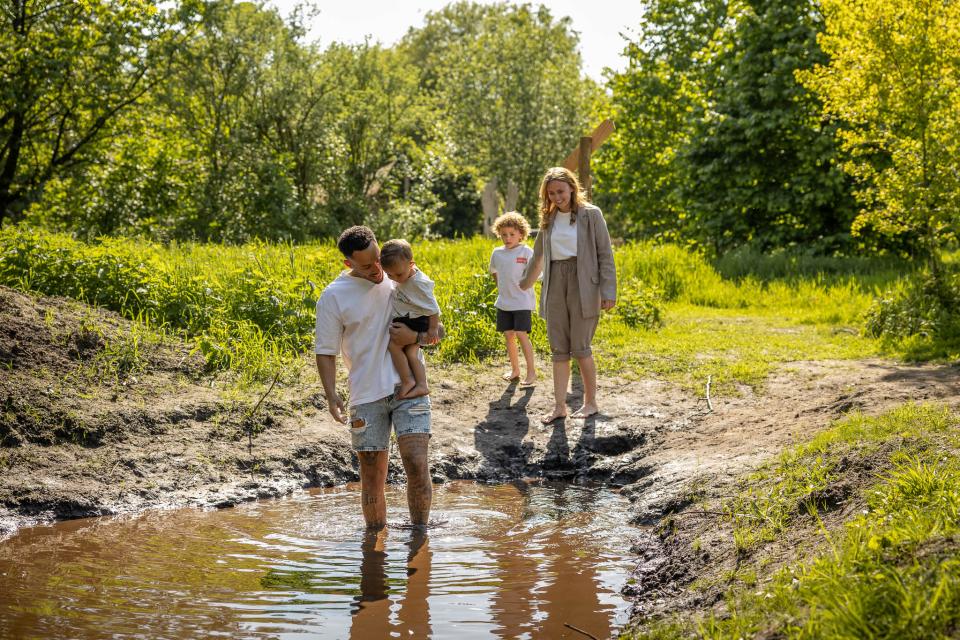 Man en vrouw met twee kinderen die door waterplas lopen in zomers landschap