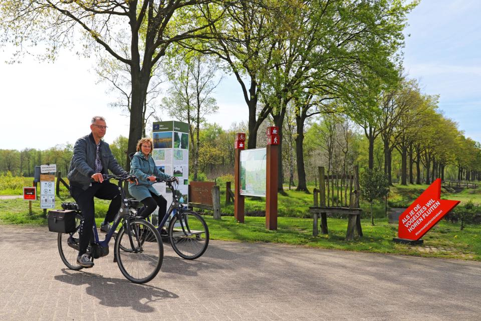 Man en vrouw op fiets bij informatieborden in landschap