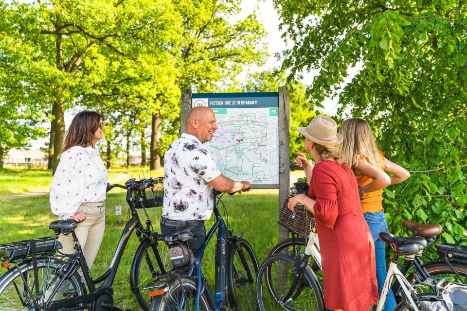 Mensen met fiets in de hand bij routebord in natuurgebied met bomen