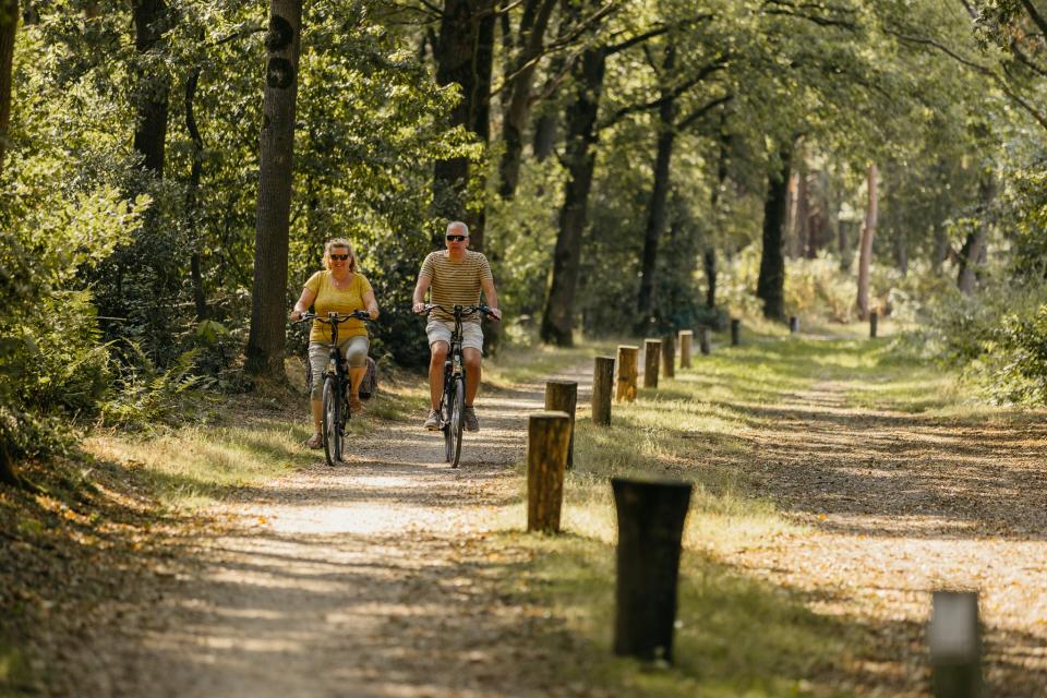 Man en vrouw op fiets over onverhard pad in boslandschap