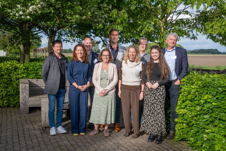 Groep mensen poseert voor foto met struiken en bomen op de achtergrond