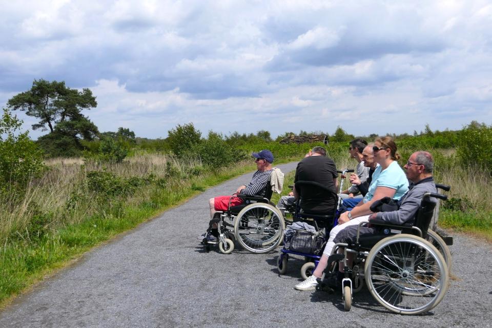 Mensen in rolstoelen op verhard pad in natuurgebied