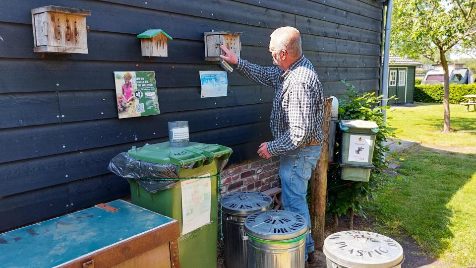 Man bij vogelhuisjes en schilderijtjes op houten buitenmuur